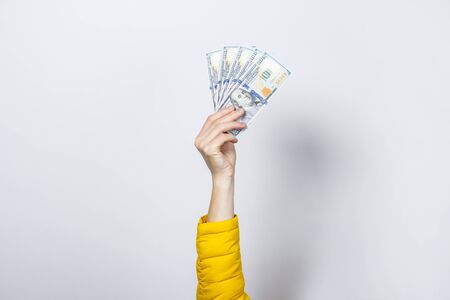 Female hand in a yellow jacket holds money on a light background. Concept rich, wealth, buy, pay, tax.の写真素材