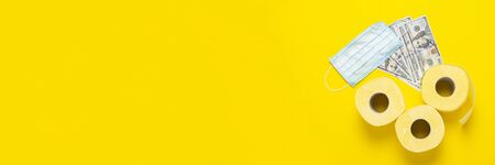 toilet paper rolls, medical mask and dollars banknotes on a yellow background. Baner. Flat lay, top...