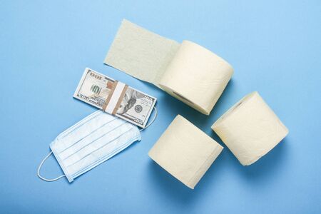 toilet paper rolls, medical mask and dollars banknotes on a blue background. Flat lay, top view....