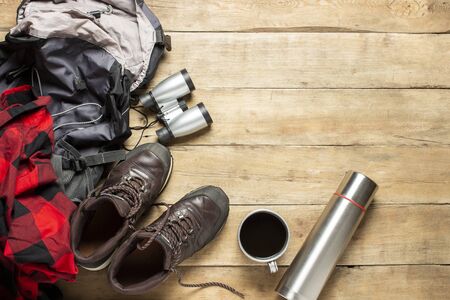 Hiking boots, binoculars, shirt, flask, backpack on a wooden background. The concept of hiking, tourism, camp, mountains, forest. Banner. Flat lay, top view.の写真素材