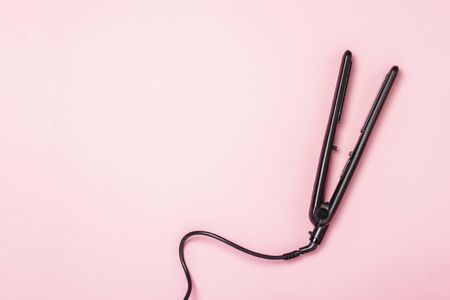 Hair straightener on a pink background. Concept of hair care, hairstyle, beauty salon, hairdresser. Flat lay, top view.の写真素材