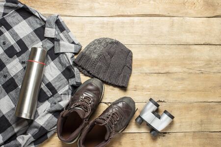 Boots for a trail, shirt, hat, binoculars on a wooden background. The concept of hiking, tourism, camp, mountains, forest. Banner. Flat lay, top view.の写真素材