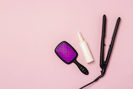 Hair straightener, comb and hair care product on a pink background. Concept of hair care, hairstyle, beauty salon, hairdresser. Flat lay, top view.の写真素材