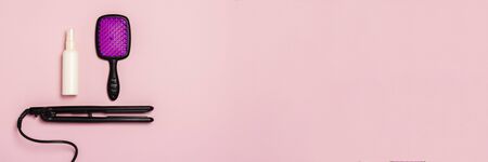 Hair straightener, comb and hair care product on a pink background. Concept of hair care, hairstyle, beauty salon, hairdresser. Flat lay, top view. Banner.の写真素材