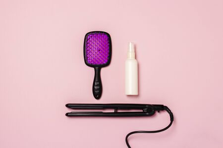 Hair straightener, comb and hair care product on a pink background. Concept of hair care, hairstyle, beauty salon, hairdresser. Flat lay, top view.の写真素材