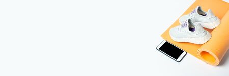 Yoga mat, sneakers and phone on a white background. Sport, training. Top view, flat lay. Banner.の写真素材