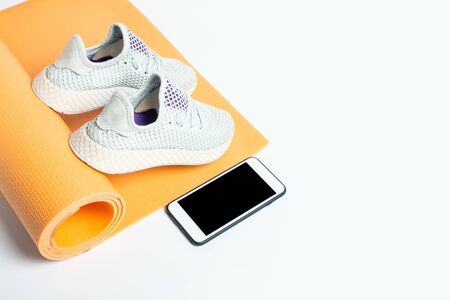 Yoga mat, sneakers and phone on a white background. Sports, yoga and training. Top view, flat lay.の写真素材
