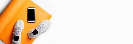 Yoga mat, sneakers and phone on a white background. Sport, training. Top view, flat lay. Banner.の写真素材