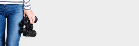 Woman holds binoculars on a light background. Only legs are visible. Banner.の写真素材