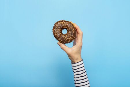 Female hand holds a donut on a blue background. Concept confectionery store, pastries, coffee shop. Banner. Flat lay, top view.の写真素材