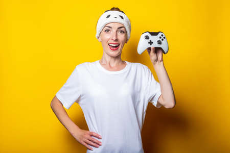 Young woman with closed eyes in white shirt holding a mascara on a yellow background.