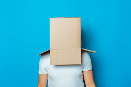 Young man in a white T-shirt with a cardboard box on his head makes a gesture with his hands on a...