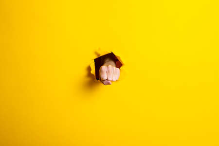 Male fist punched a hole in a yellow background. Blow, strength, masculine strengthの写真素材