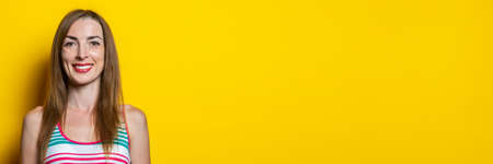 Friendly smiling young woman in a striped dress on a yellow background. Banner.の写真素材