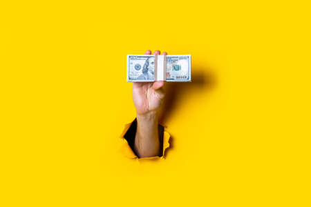 Female hand holds horizontally a bundle of money bills on a yellow backgroundの写真素材