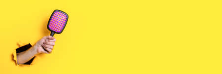 Female hand holds a large hairbrush on a yellow background. Hair accessories. Banner
