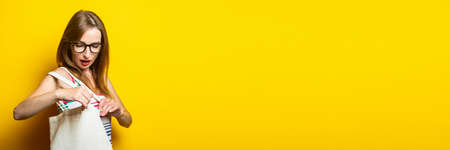 Surprised young woman looking into linen bag with purchases on yellow background. Bannerの写真素材