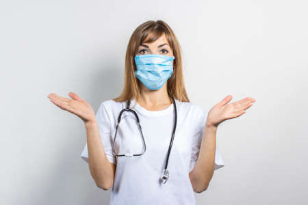 Young woman in a medical mask and a stethoscope makes a hand gesture on a light background. Banner. Concept doctor, high level medical medicine, vaccination, visit to the doctor.の写真素材