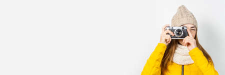 Young woman in a yellow down jacket and hat holds a camera in her hands and takes a picture on a...
