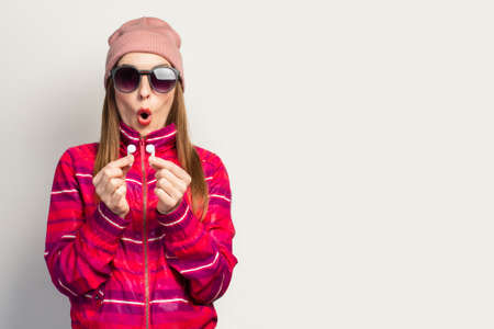Emotional Young woman in glasses, a hat and a pink sports jacket with a surprised face holds...