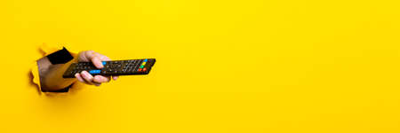 Female hand presses the button on the TV remote control on a bright yellow background. Bannerの写真素材