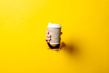 Female hand holding a paper cup of coffee on a bright yellow backgroundの写真素材