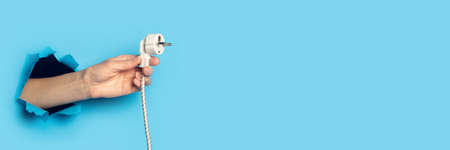 Female hand holding the plug on a bright blue background. Banner