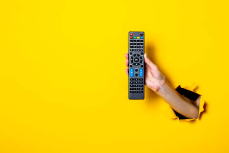 Female hand holding a TV remote control on a bright yellow background.の写真素材