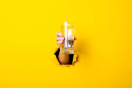 Female hand holding a glass of water on a bright yellow background.