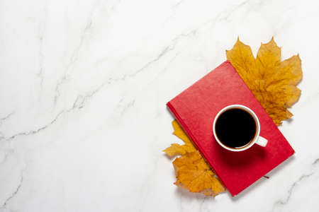 Cup with coffee or tea, yellow autumn leaves and a book on a marble table. The concept of breakfast, education, knowledge, reading books, leisure, autumn. Flat lay, top view.の写真素材