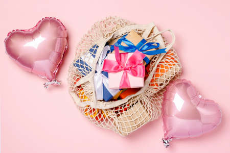 Shopping Bag with gift and heart shaped air balloon on a pink background. Gifts concept for family, loved ones, christmas, valentines day. Banner. Flat lay, top view.の写真素材