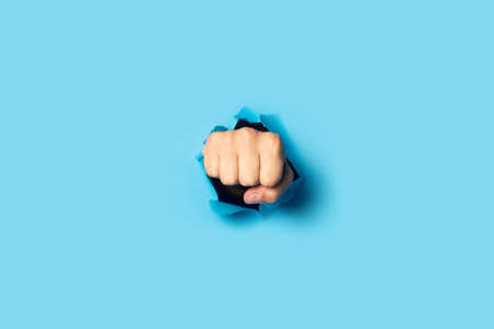 Male fist punches a wall on a blue background. Banner. Breakout gesture, break.