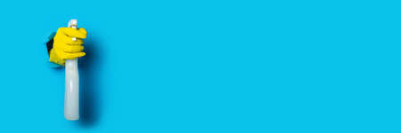 Hand in yellow gloves holding spray on a bright blue background. Bannerの写真素材