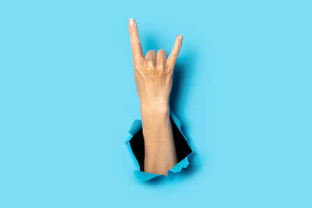 Female hand making a rock and roll gesture, party, goat on a blue background. Banner.の写真素材