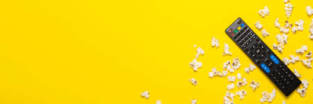TV remote control, TV tuner or audio system and popcorn on a yellow background. Concept series,...