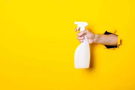 Hand holds spray with cleaning agent or water on yellow background.の写真素材