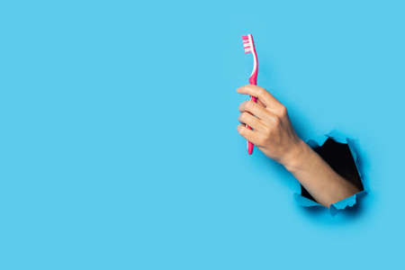 Female hand holding a toothbrush on a bright blue background.の写真素材