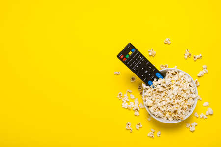 TV remote control, TV tuner lie in a bowl with popcorn on a yellow background. Concept series, film, sports. Banner. Flat lay, top view.の写真素材