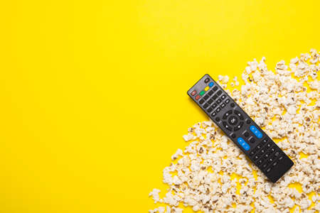 TV remote control, TV tuner or audio system and popcorn on a yellow background. Concept series, film, sports. Banner. Flat lay, top view.の写真素材