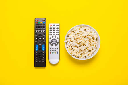 Two remotes from the TV, TV tuner and a bowl of popcorn on a yellow background. Concept series, film, sports. Banner. Flat lay, top view.の写真素材