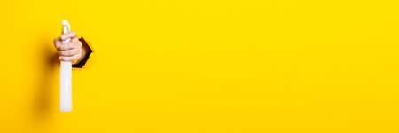 Hand holds spray with cleaning agent or water on yellow background.