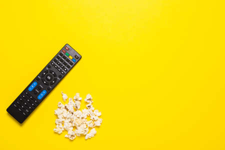 TV remote control, TV tuner or audio system and popcorn on a yellow background. Concept series,...