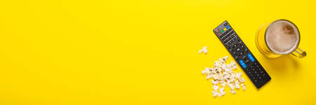 Remote control from a TV or TV tuner, a glass of beer and popcorn on a yellow background. Concept...