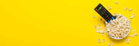 TV remote control, TV tuner lie in a bowl with popcorn on a yellow background. Concept series, film, sports. Banner. Flat lay, top view.の写真素材