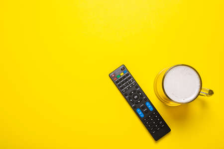 Remote control from the TV or TV tuner, a glass of beer on a yellow background. Concept series, film, sports. Banner. Flat lay, top view.の写真素材
