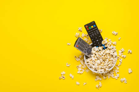 Two remotes from the TV, TV tuner lie in a bowl with popcorn on a yellow background. Concept series, film, sports. Banner. Flat lay, top view.の写真素材