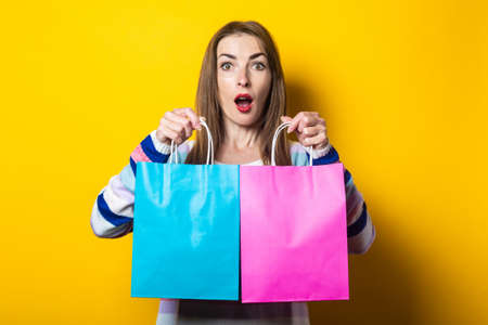 Young woman looks into the phone and holds shopping bags with purchases on a yellow background. Banner.の写真素材