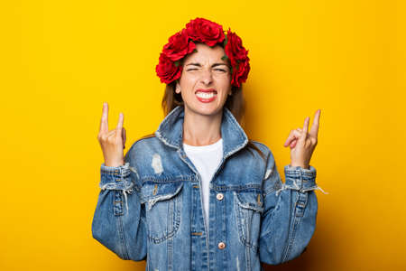 Young woman shows a gesture Cool, Let's rock this party, in a denim jacket and a wreath of red...
