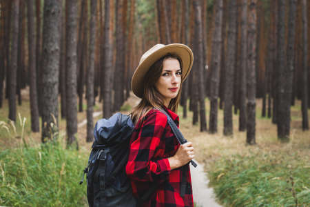Young woman in hat, red shirt and backpack in the forest. Hike in the forest.