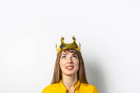Young woman in a yellow jacket and a gold crown on a light background. Emotion laughter, surprise, kiss. Concept of a queen, luck, the best, win, victory. Banner.の写真素材